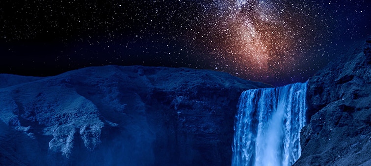 Közelkép egy éjszakai vízesésről, az égbolton egy galaxis világító csillagaival