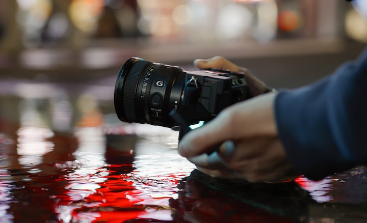 Kép egy pocsolya fölé tartott α7C R fényképezőgépről, amelyre FE 16 mm F1.8 G objektív van felszerelve
